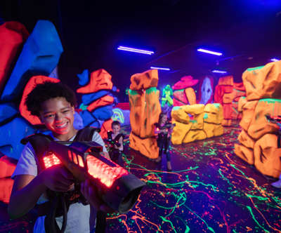 Boy playing laser tag with people behind him and a neon background